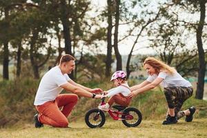 mãe e pai ensinando filha a andar de bicicleta ao ar livre foto