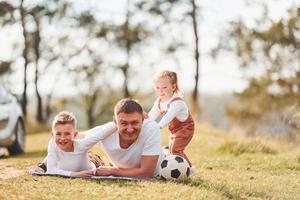 pai com sua filhinha e filho deitado no chão ao ar livre perto da floresta foto