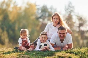 com bola de futebol. família feliz deitado ao ar livre perto da floresta. com filha e filho foto