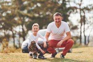 jogando futebol. pai com seu filho passando o fim de semana juntos ao ar livre perto da floresta durante o dia foto