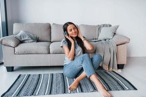 jovem mulher bonita em roupas casuais sentada em casa sozinha e ouvindo música em fones de ouvido foto