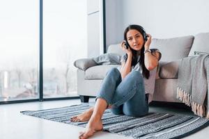 jovem mulher bonita em roupas casuais sentada em casa sozinha e ouvindo música em fones de ouvido foto