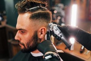close-up vista do jovem barbudo que sentado e cortando o cabelo na barbearia foto