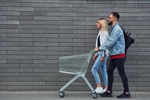 com carrinho de compras. jovem elegante com mulher em roupas casuais ao ar livre juntos. concepção de amizade ou relacionamentos foto