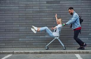 se divertindo e andando de carrinho de compras. jovem elegante com mulher em roupas casuais ao ar livre juntos. concepção de amizade ou relacionamentos foto