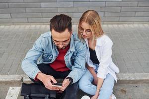 usando telefone. jovem elegante com mulher em roupas casuais sentados juntos ao ar livre. concepção de amizade ou relacionamentos foto