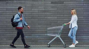 com carrinho de compras. jovem elegante com mulher em roupas casuais ao ar livre juntos. concepção de amizade ou relacionamentos foto