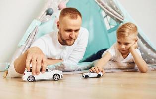 com carros de brinquedo. pai e seus jovens passando tempo juntos dentro de casa perto da tenda foto