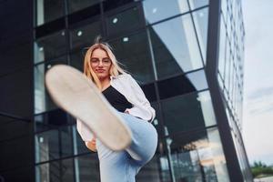 linda loira em roupas casuais está ao ar livre durante o dia ensolarado contra a construção de negócios foto