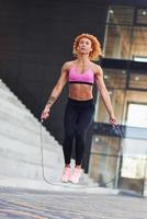 jovem ruiva europeia em roupas esportivas pulando com corda ao ar livre foto