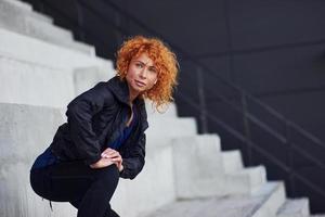 jovem ruiva europeia em roupas esportivas fazendo exercícios na escada ao ar livre foto