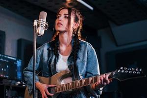 jovem bela artista feminina com violão cantando e ensaiando em um estúdio de gravação foto