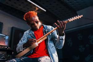 toca violão. jovem artista afro-americana ensaiando em um estúdio de gravação foto