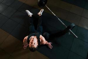 vista superior do homem forte em roupas esportivas que sentado no chão e faz uma pausa no ginásio foto