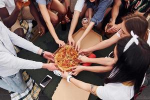 com deliciosas pizzas. grupo de jovens em roupas casuais faz uma festa no telhado juntos durante o dia foto