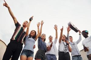 de pé alto e olhando para o céu nublado. grupo de jovens em roupas casuais faz uma festa no telhado juntos durante o dia foto