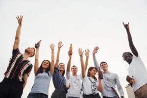 de pé alto e olhando para o céu nublado. grupo de jovens em roupas casuais faz uma festa no telhado juntos durante o dia foto