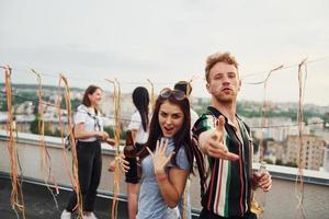 casal feliz. grupo de jovens em roupas casuais faz uma festa no telhado juntos durante o dia foto