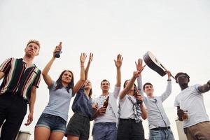 de pé alto e olhando para o céu nublado. grupo de jovens em roupas casuais faz uma festa no telhado juntos durante o dia foto