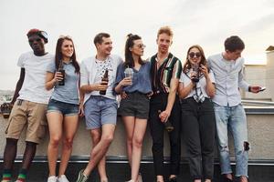 de pé com álcool na beira do telhado. grupo de jovens em roupas casuais fazem uma festa juntos durante o dia foto