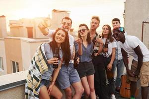 tirando selfie. belo sol. grupo de jovens em roupas casuais faz uma festa no telhado juntos durante o dia foto