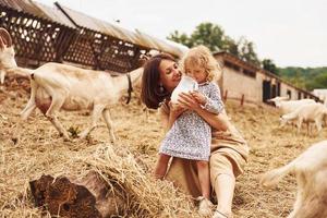 jovem mãe com sua filha está na fazenda no verão com cabras foto