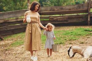 leite natural fresco. jovem mãe com sua filha está na fazenda no verão com cabras foto