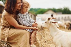 leite natural fresco. jovem mãe com sua filha está na fazenda no verão com cabras foto