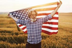 homem sênior patriótico em pé no campo com a bandeira dos eua. concepção de liberdade foto