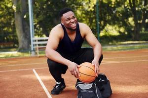 senta-se com bolsa preta e se preparando para o jogo. homem afro-americano joga basquete na quadra ao ar livre foto