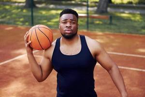 homem afro-americano em pé com bola na quadra ao ar livre foto