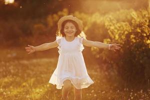 menina feliz em vestido branco divirta-se ao ar livre no prado no verão foto