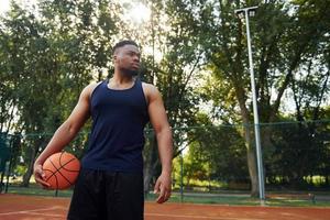 homem afro-americano em pé com bola na quadra ao ar livre foto