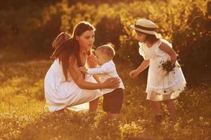 alegre família de mãe, filho e filha passar o tempo livre no campo em dia ensolarado de verão foto