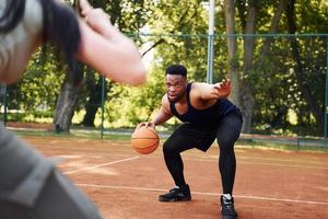 homem afro-americano com garota joga basquete na quadra ao ar livre foto