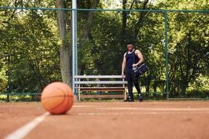 belas árvores verdes no fundo. homem afro-americano joga basquete na quadra ao ar livre foto