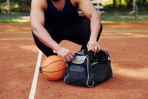 senta-se com bolsa preta e se preparando para o jogo. homem afro-americano joga basquete na quadra ao ar livre foto