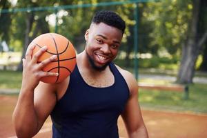 homem afro-americano em pé com bola na quadra ao ar livre foto