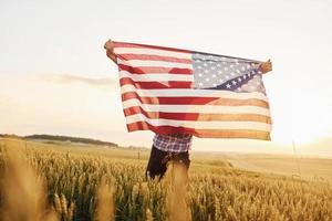 segurando a bandeira dos eua nas mãos. homem estiloso sênior patriótico com cabelos grisalhos e barba no campo agrícola foto