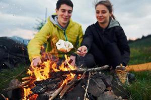 casal com marshmallow perto da fogueira. majestosas montanhas dos cárpatos. bela paisagem de natureza intocada foto