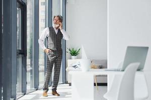 chefe em roupas formais trabalha no escritório. homem moderno elegante sênior com cabelos grisalhos e barba dentro de casa foto