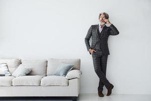 posando para a câmera. homem moderno elegante sênior com cabelos grisalhos e barba dentro de casa foto