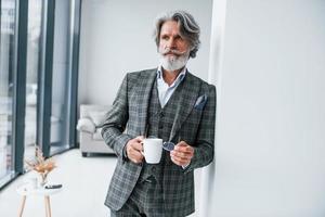 parado na sala. homem moderno elegante sênior com cabelos grisalhos e barba dentro de casa foto