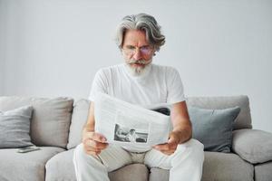 senta no sofá. homem moderno elegante sênior com cabelos grisalhos e barba dentro de casa foto