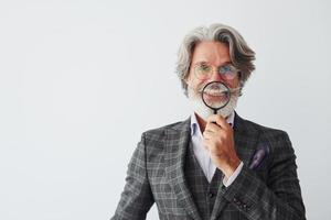 se divertindo com lupa. homem moderno elegante sênior com cabelos grisalhos e barba dentro de casa foto