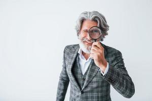 se divertindo com lupa. homem moderno elegante sênior com cabelos grisalhos e barba dentro de casa foto