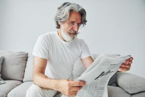 senta no sofá. homem moderno elegante sênior com cabelos grisalhos e barba dentro de casa foto