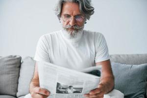 senta no sofá. homem moderno elegante sênior com cabelos grisalhos e barba dentro de casa foto