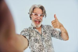 turista faz selfie. homem moderno elegante sênior com cabelos grisalhos e barba dentro de casa foto