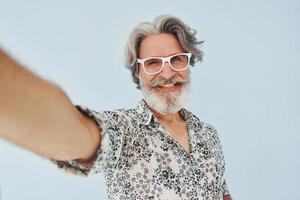 turista faz selfie. homem moderno elegante sênior com cabelos grisalhos e barba dentro de casa foto